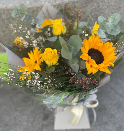 Golden Glow - Brighten someone's day with the `Golden Glow` arrangement, featuring a stunning sunflower mix with seasonal blooms. Complemented by lush green foliage, this arrangement brings a touch of nature's radiant beauty into any space.